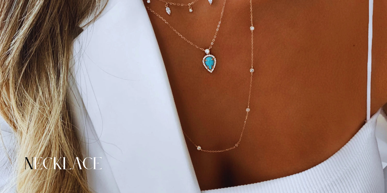 Close-up of a woman wearing layered gold necklaces, one with a turquoise teardrop pendant and small gemstones, paired with a white top and blazer. The word "NECKLACE" appears in the corner.
