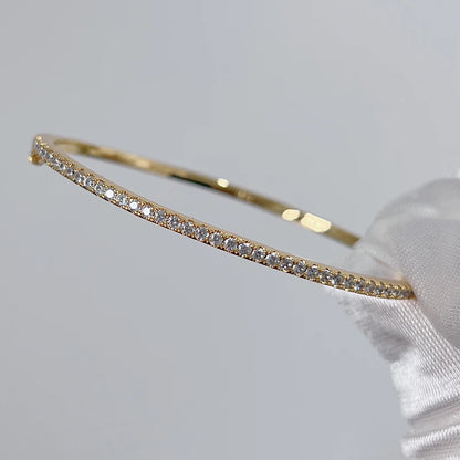 Gleaming gold bangle with a sparkling zircon stone centerpiece, showcasing a minimalist, unisex round design.